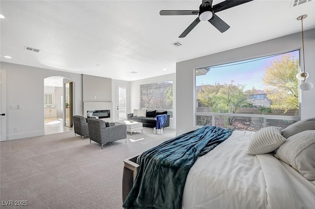 bedroom with ceiling fan, light colored carpet, ensuite bathroom, and a large fireplace