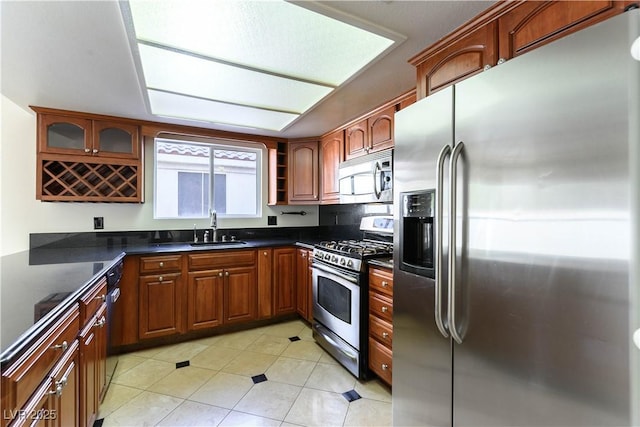 kitchen featuring stainless steel appliances, sink, dark stone counters, and light tile patterned floors