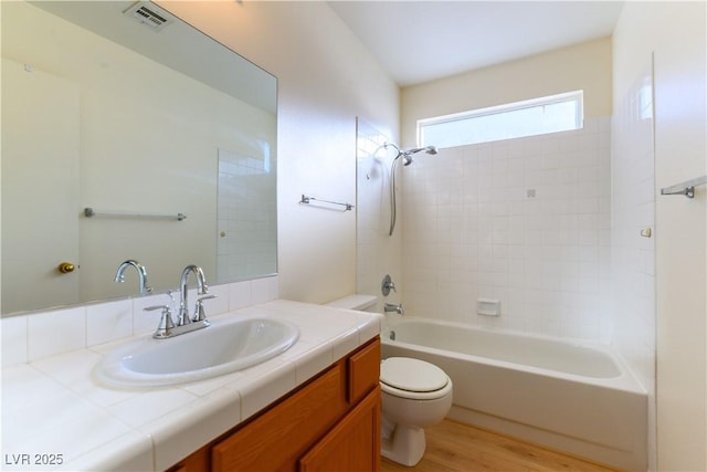 full bathroom with tiled shower / bath combo, vanity, wood-type flooring, and toilet