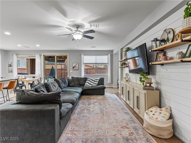 living room featuring wooden walls, light hardwood / wood-style floors, and ceiling fan