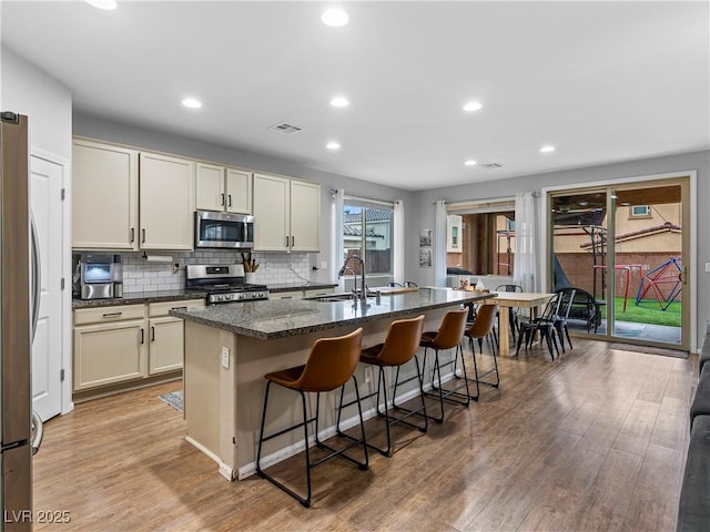 kitchen with sink, a breakfast bar area, stainless steel appliances, an island with sink, and dark stone counters