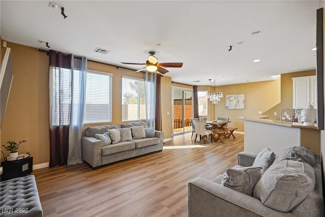 living room with ceiling fan with notable chandelier and light hardwood / wood-style floors