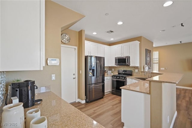 kitchen with sink, white cabinets, light stone counters, kitchen peninsula, and stainless steel appliances