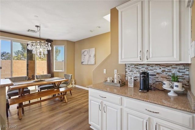 kitchen featuring light stone counters, backsplash, hanging light fixtures, and white cabinets