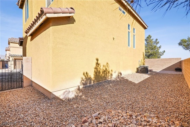 view of side of home with a tile roof, fence, cooling unit, and stucco siding