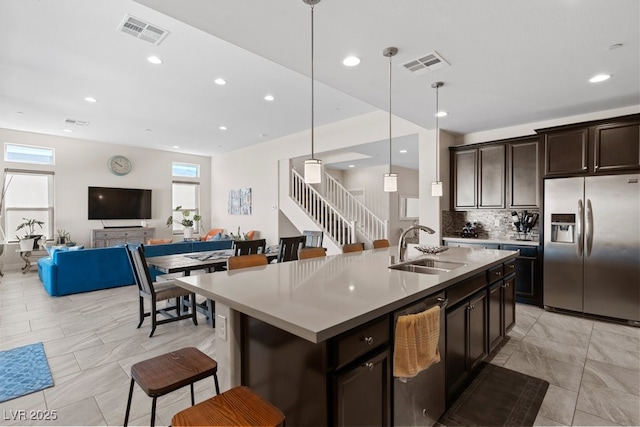 kitchen featuring dishwashing machine, hanging light fixtures, light countertops, stainless steel refrigerator with ice dispenser, and an island with sink