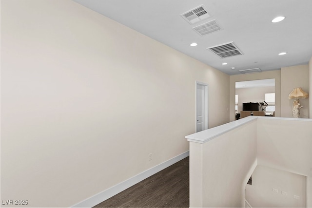 hallway featuring dark wood-style flooring, baseboards, visible vents, and an upstairs landing