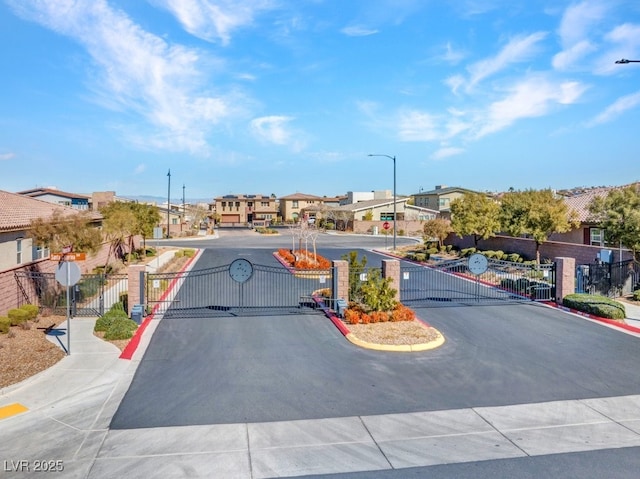 view of street with curbs, street lighting, a gated entry, and a residential view