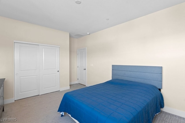 bedroom with a closet, light colored carpet, and baseboards