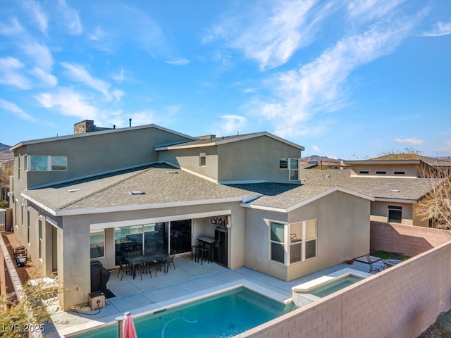 rear view of property with stucco siding, roof with shingles, a fenced backyard, and an in ground hot tub