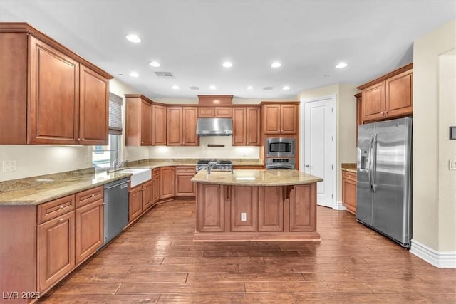 kitchen featuring dark wood-type flooring, sink, light stone counters, a center island, and appliances with stainless steel finishes