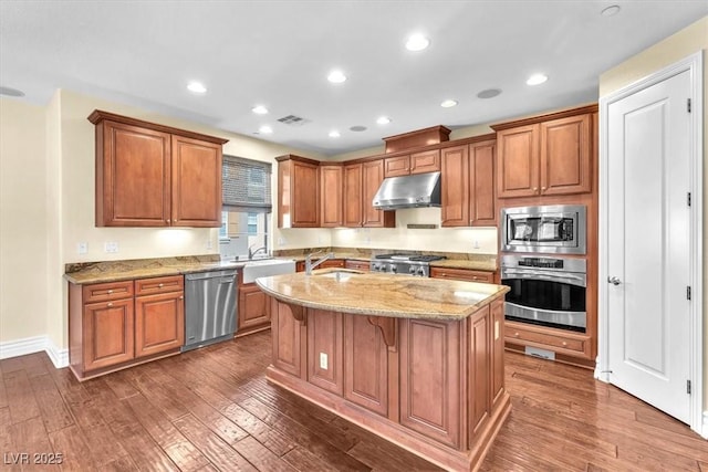 kitchen featuring a center island, appliances with stainless steel finishes, dark hardwood / wood-style floors, a kitchen breakfast bar, and light stone countertops