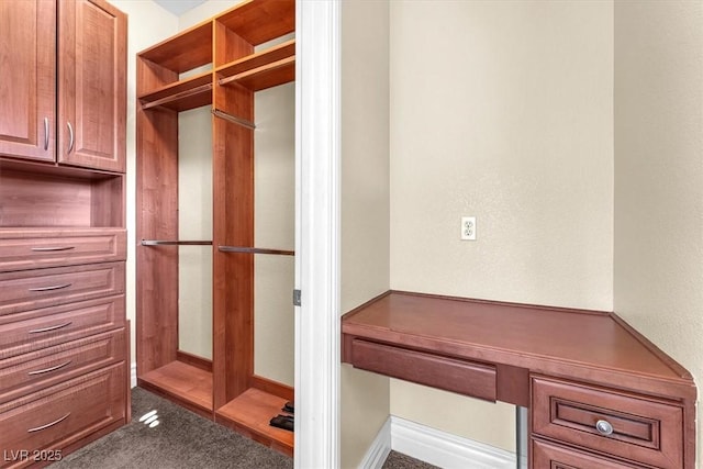 walk in closet with dark colored carpet and built in desk