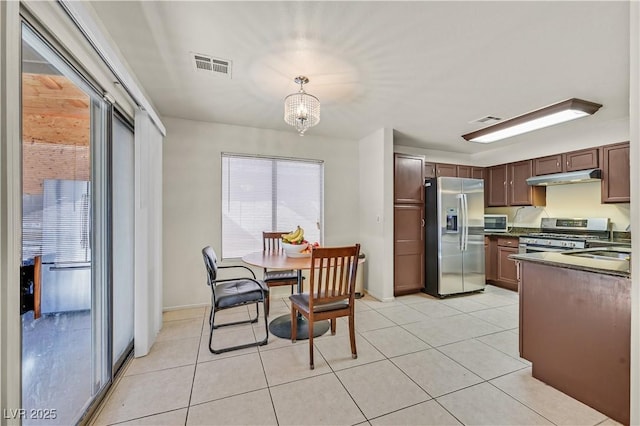 kitchen with light tile patterned floors, under cabinet range hood, stainless steel appliances, visible vents, and dark countertops