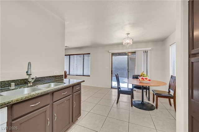 kitchen with a notable chandelier, light tile patterned floors, a sink, dark stone countertops, and baseboards