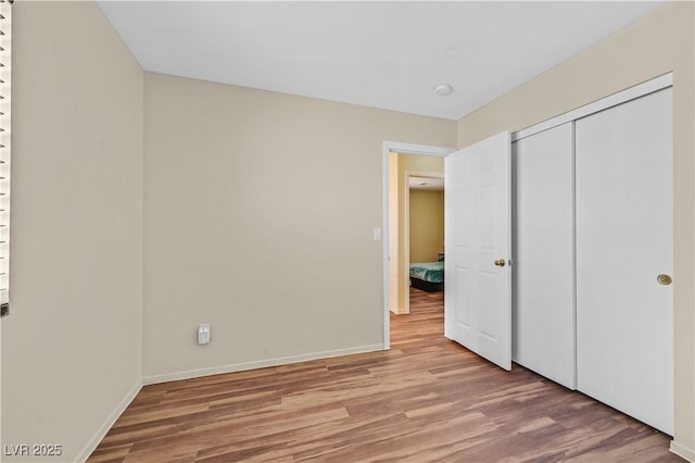 unfurnished bedroom featuring light wood-type flooring, baseboards, and a closet