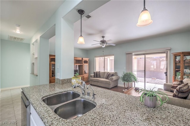 kitchen featuring pendant lighting, stainless steel dishwasher, light stone countertops, and sink