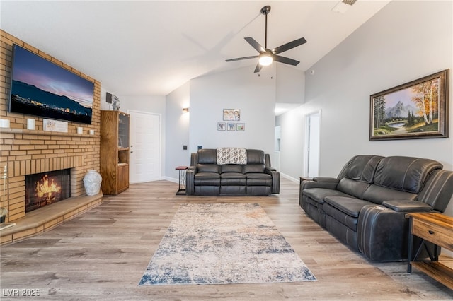 living room with ceiling fan, high vaulted ceiling, light hardwood / wood-style floors, and a brick fireplace