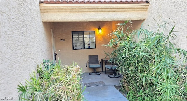 entrance to property featuring a patio area, a tiled roof, and stucco siding