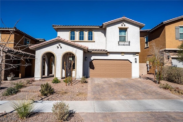 mediterranean / spanish house with an attached garage, a tiled roof, decorative driveway, and stucco siding