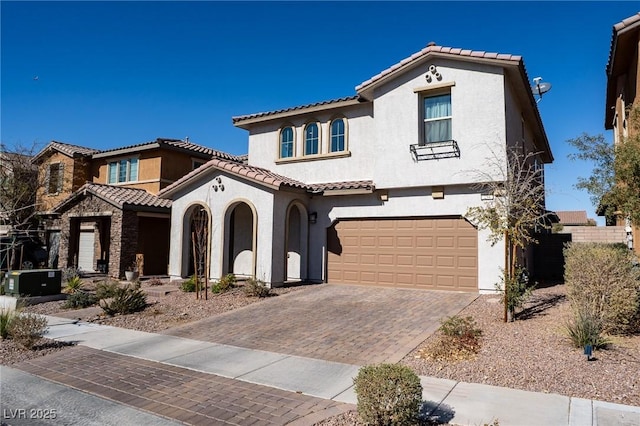 mediterranean / spanish house featuring an attached garage, a tile roof, decorative driveway, and stucco siding