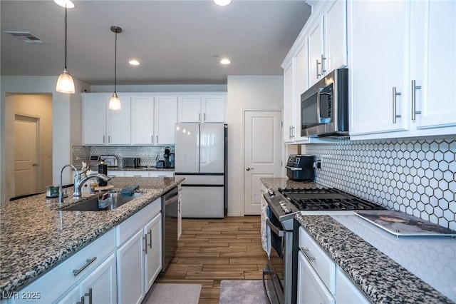 kitchen with pendant lighting, sink, white cabinetry, dark stone countertops, and stainless steel appliances