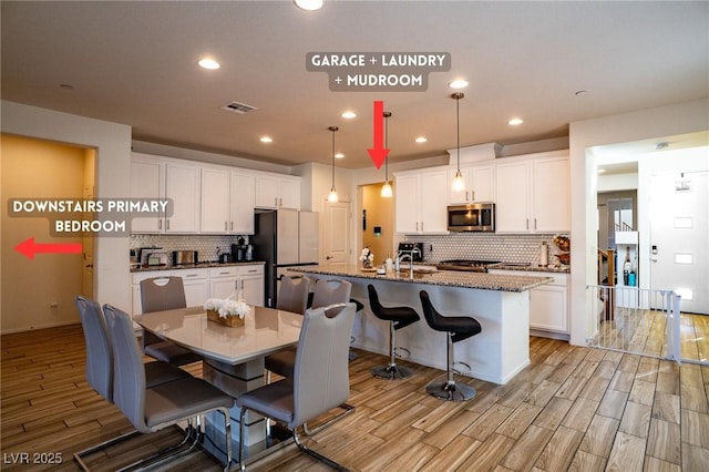 kitchen with visible vents, white cabinets, stainless steel microwave, freestanding refrigerator, and wood finish floors