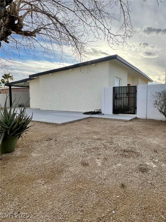 view of property exterior with a patio, fence, a gate, and stucco siding