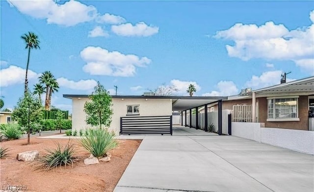 view of front facade featuring fence, an attached carport, concrete driveway, and stucco siding