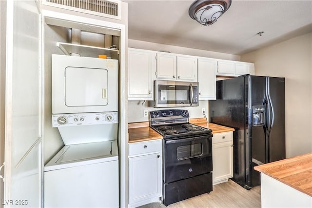 kitchen featuring wood counters, stacked washer / drying machine, black appliances, light hardwood / wood-style floors, and white cabinets