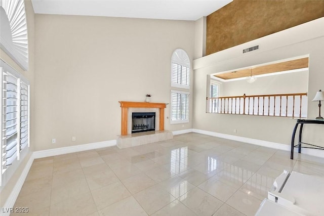 unfurnished living room featuring light tile patterned flooring, a towering ceiling, and a tile fireplace