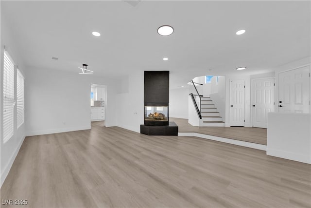 unfurnished living room featuring a multi sided fireplace and light hardwood / wood-style floors