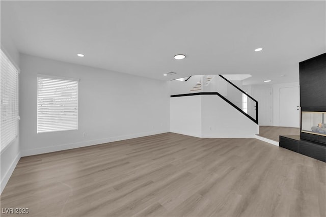 unfurnished living room with a multi sided fireplace and light wood-type flooring