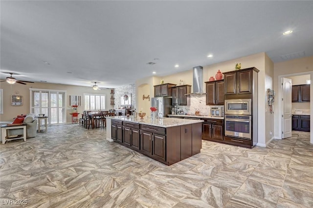 kitchen featuring appliances with stainless steel finishes, wall chimney range hood, a kitchen island with sink, and dark brown cabinets