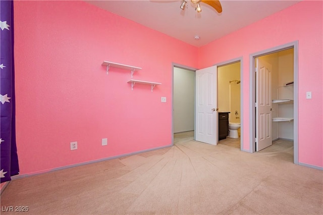 unfurnished bedroom with ceiling fan, light colored carpet, ensuite bath, and a walk in closet