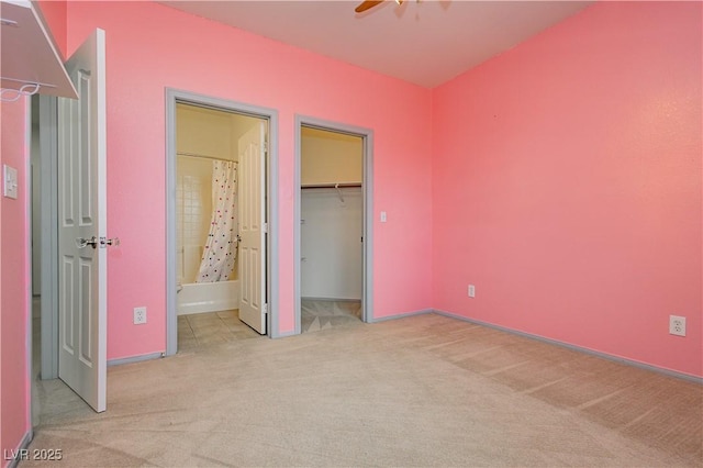 unfurnished bedroom featuring ensuite bathroom, a walk in closet, ceiling fan, light carpet, and a closet