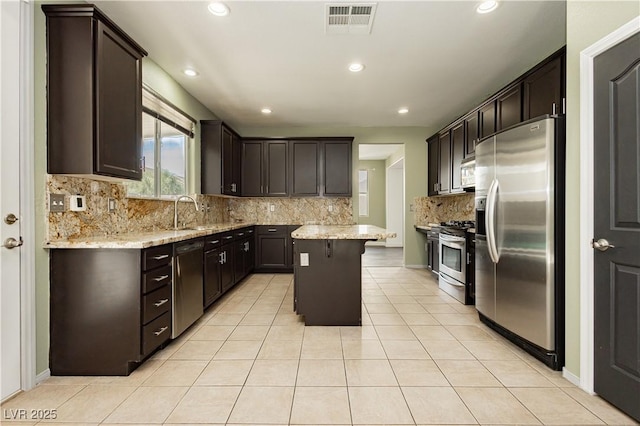 kitchen featuring light stone countertops, appliances with stainless steel finishes, a center island, and light tile patterned flooring