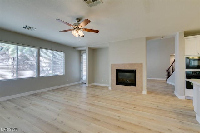 unfurnished living room with a tile fireplace, ceiling fan, and light hardwood / wood-style floors