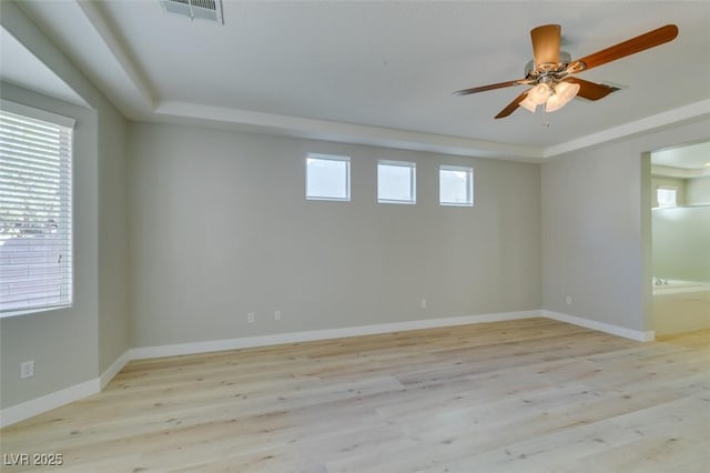 empty room with a wealth of natural light, light hardwood / wood-style flooring, a raised ceiling, and ceiling fan