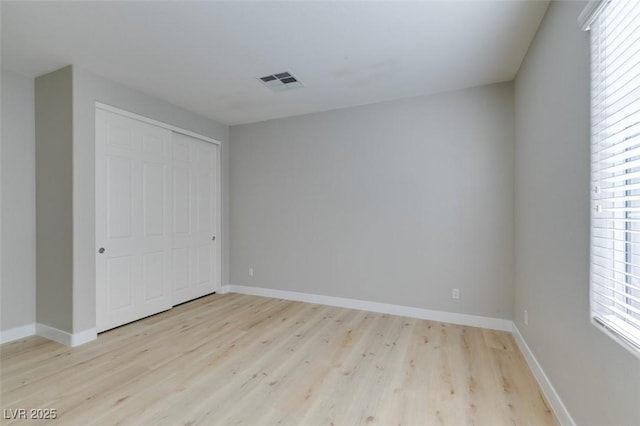 unfurnished bedroom featuring multiple windows, light hardwood / wood-style floors, and a closet