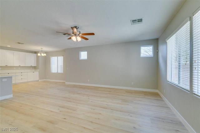 unfurnished living room with a healthy amount of sunlight, ceiling fan with notable chandelier, and light hardwood / wood-style flooring