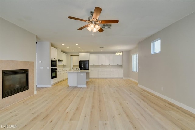 kitchen with white cabinetry, hanging light fixtures, black appliances, an island with sink, and light hardwood / wood-style floors