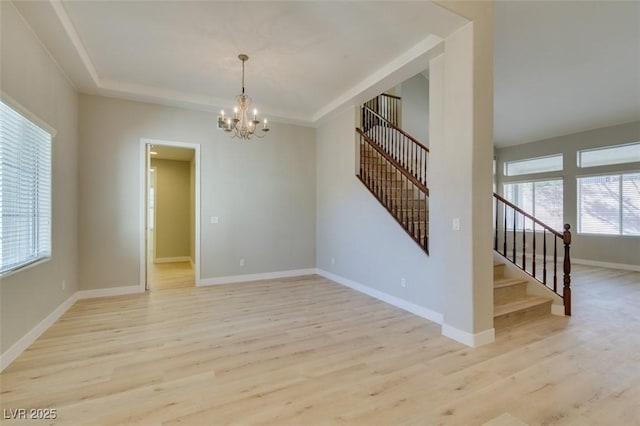 empty room featuring an inviting chandelier, a tray ceiling, and light wood-type flooring