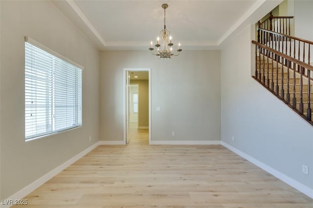 empty room featuring an inviting chandelier, a raised ceiling, and light wood-type flooring