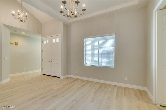 entrance foyer featuring a raised ceiling, lofted ceiling, a notable chandelier, and light hardwood / wood-style floors