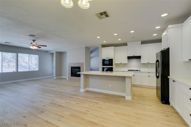 kitchen with an island with sink, white cabinets, ceiling fan, black appliances, and light wood-type flooring