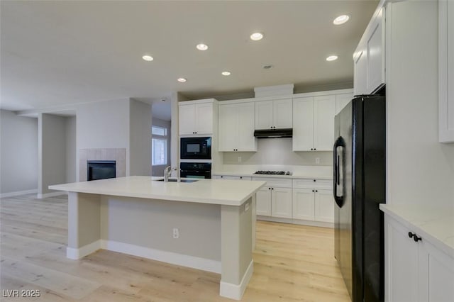 kitchen with white cabinetry, sink, a kitchen island with sink, light hardwood / wood-style floors, and black appliances