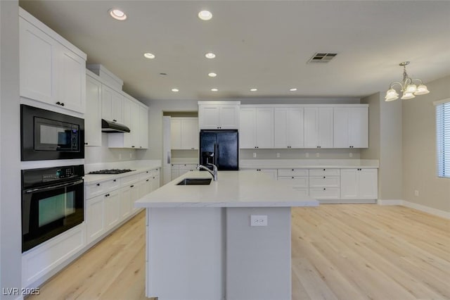 kitchen with pendant lighting, sink, white cabinets, a kitchen island with sink, and black appliances