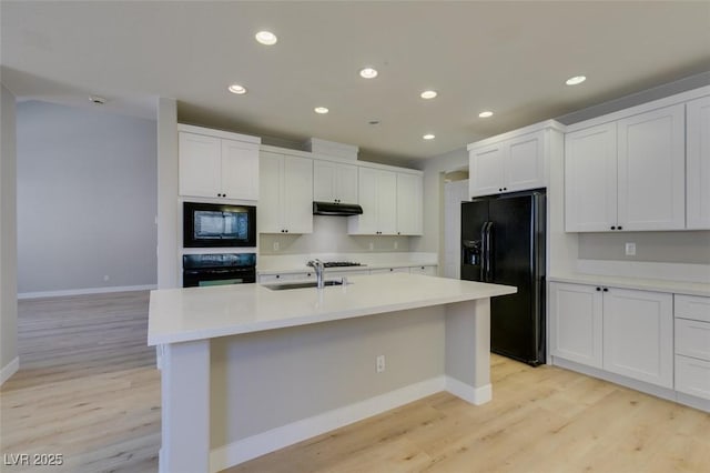 kitchen featuring sink, light hardwood / wood-style floors, black appliances, an island with sink, and white cabinets