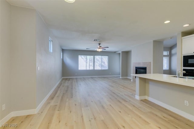 unfurnished living room featuring a tiled fireplace, sink, ceiling fan, and light hardwood / wood-style flooring